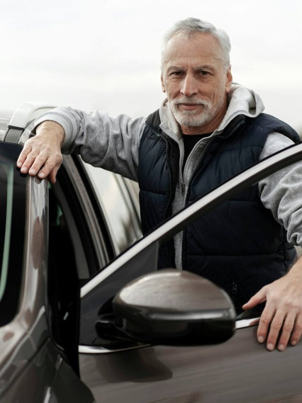 Close-up confident senior man standing by his new car in the outdoors parking lot of a dealership