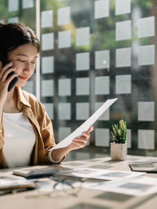 Young asian accountant calling marketing consultants and using laptop computer to analyze sales