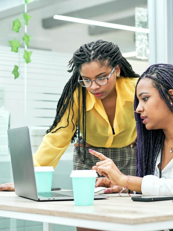 Two young black women reviewing analytical data on various electronic devices.