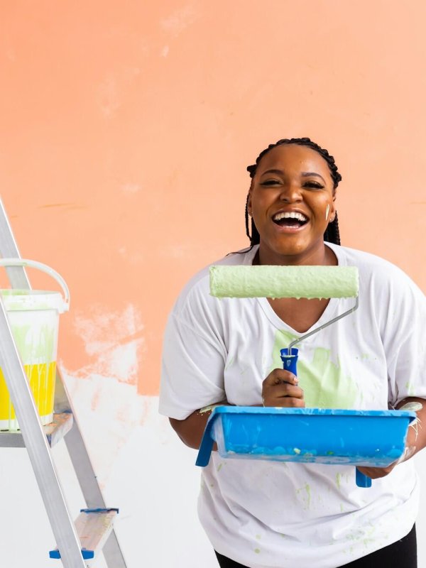 Smiling african american woman painting interior wall of home. Renovation, repair and redecoration