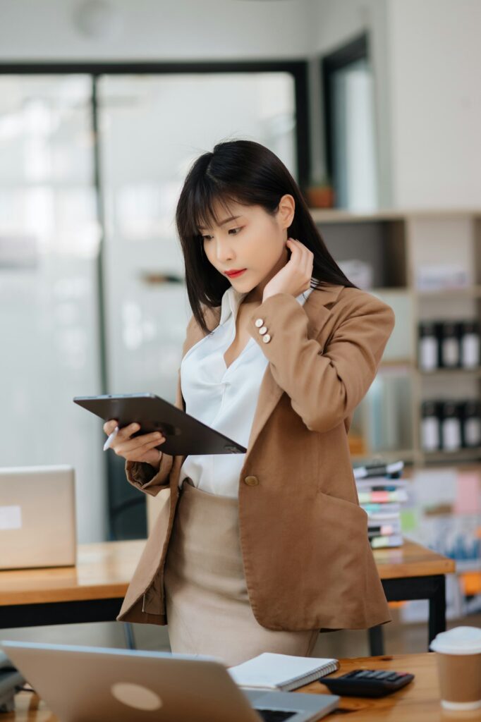 Successful Asian Businesswoman Analyzing Finance on Tablet and Laptop at modern Office Desk