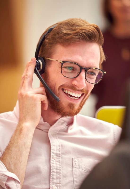 Businessman Wearing Headset Talking To Caller In Busy Customer Services Centre